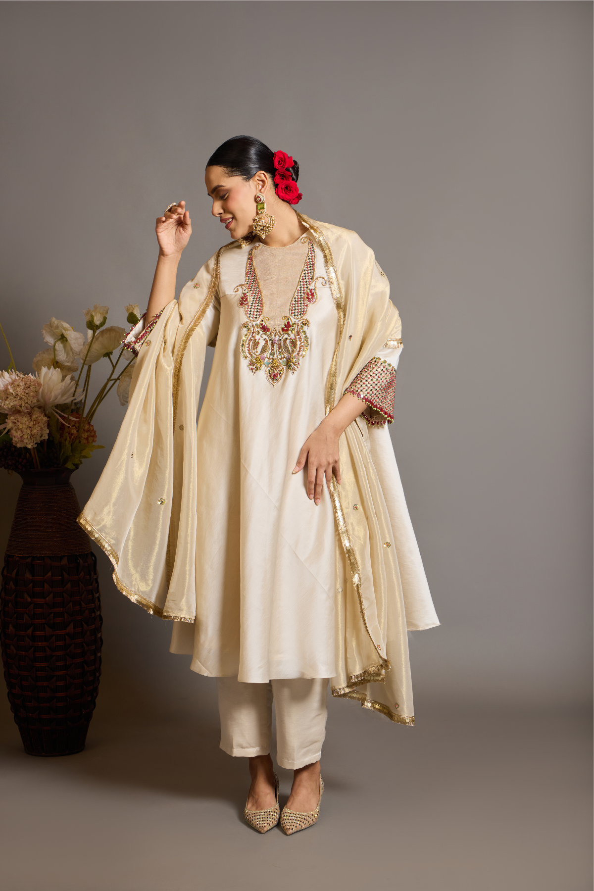 An elegant ivory kurta set crafted in a lustrous fabric, paired with tapered trousers and a fluid dupatta. Features exquisite multicolour handcrafted embroidery with ornate paisley-inspired motifs. A delicately embellished dupatta with gold edging and richly embroidered cuffs completes the look . Shop Now!