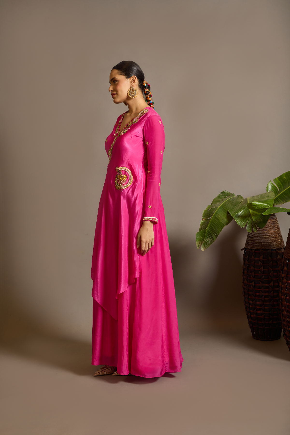 A striking fuchsia-pink Anarkali in a fluid lustrous fabric, designed with an elegant layered flare. Intricate paisley and floral embroidery in multicoloured threadwork enhances the neckline and waist. Handcrafted statement tassels adds festive charm. A vibrant contemporary Silhoutte perfect for festive soirées. Shop Now!