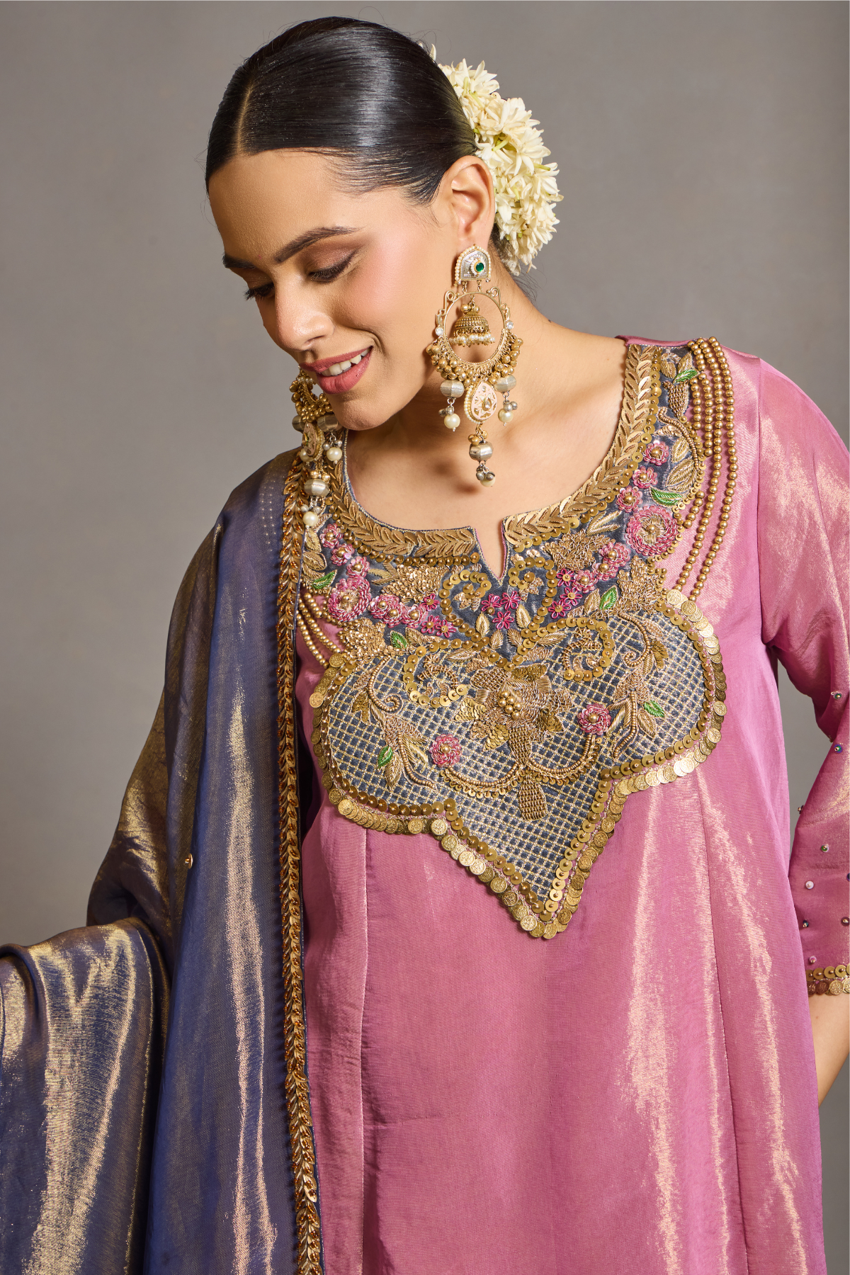 A luminous rose-pink kurta and flared palazzo set crafted in rich,metallic-finish fabric. Featuring an ornate multicolour embroidered neckline with intricate zardozi inspired detailing. Paired with a contrasting deep-blue dupatta finished with elegant gold borders. A festive ensemble that beautifully blends contemporary ease with traditional opulence. Shop Now!