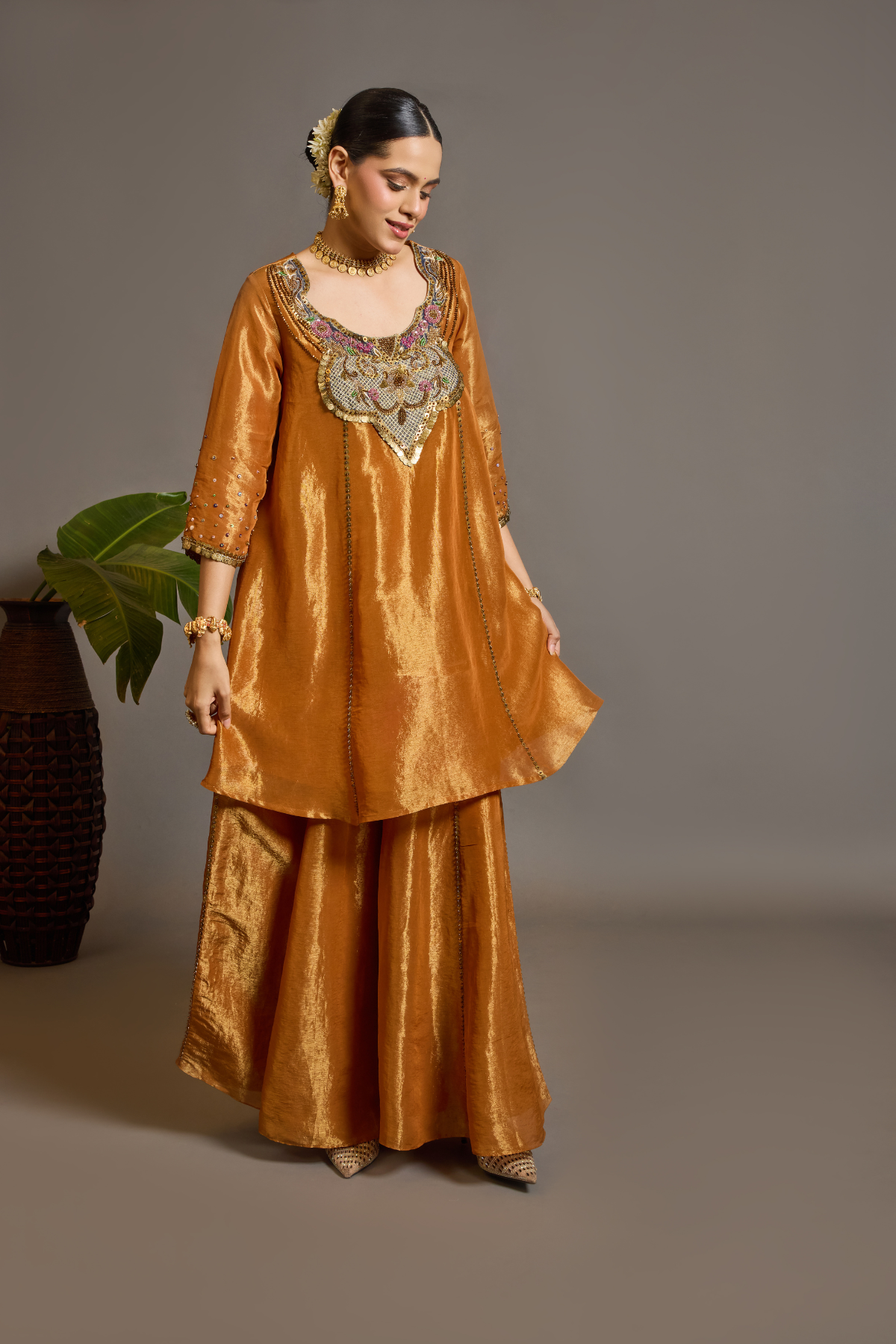 A luminous burnt-orange kurta in a rich metallic finish, elevated with an ornate handcrafted embroidered yoke. The statement neckline features intricate multicolour florals, paisleys,sequins and antique-gold detailing. Layered with a deep-navy blue metallic dupatta finished with ornate borders and delicate embellishment. A festive look that blends contemporary glamour with traditional Indian craftsmanship. Shop Now!