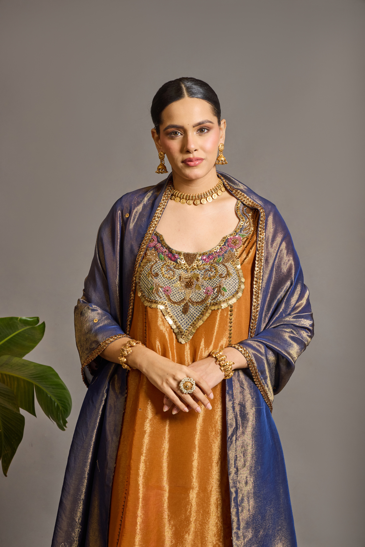 A luminous burnt-orange kurta in a rich metallic finish, elevated with an ornate handcrafted embroidered yoke. The statement neckline features intricate multicolour florals, paisleys,sequins and antique-gold detailing. Layered with a deep-navy blue metallic dupatta finished with ornate borders and delicate embellishment. A festive look that blends contemporary glamour with traditional Indian craftsmanship. Shop Now!