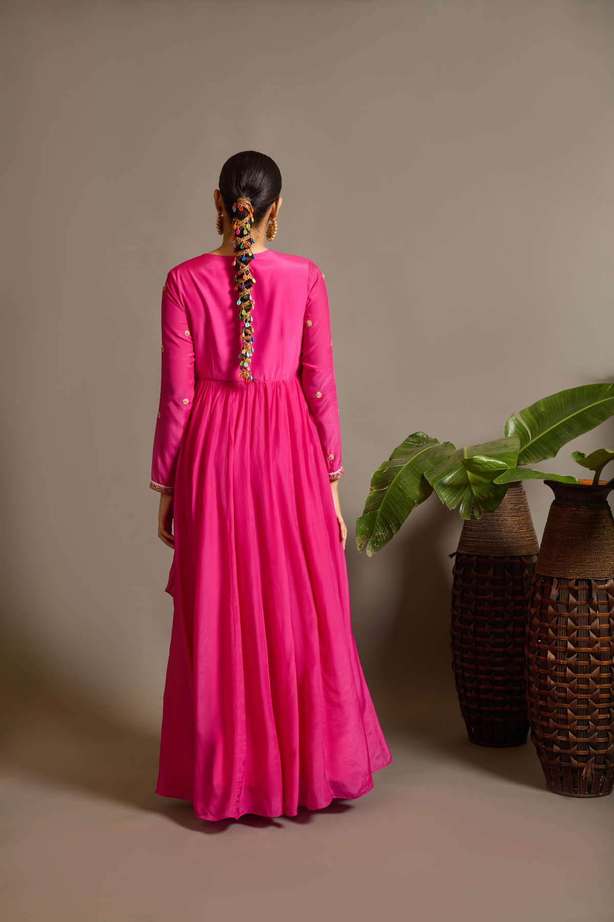 A striking fuchsia-pink Anarkali in a fluid lustrous fabric, designed with an elegant layered flare. Intricate paisley and floral embroidery in multicoloured threadwork enhances the neckline and waist. Handcrafted statement tassels adds festive charm. A vibrant contemporary Silhoutte perfect for festive soirées. Shop Now!