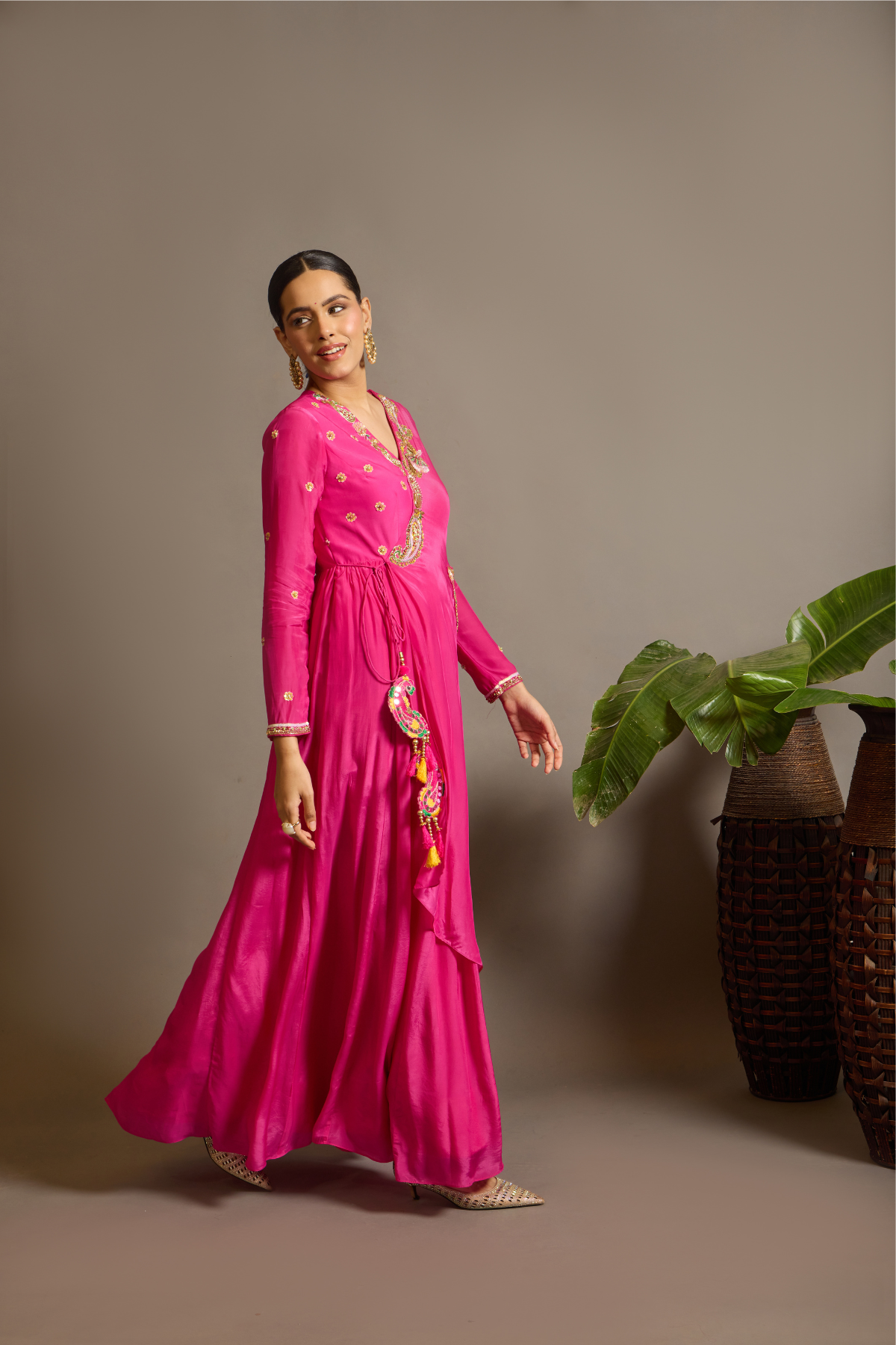 A striking fuchsia-pink Anarkali in a fluid lustrous fabric, designed with an elegant layered flare. Intricate paisley and floral embroidery in multicoloured threadwork enhances the neckline and waist. Handcrafted statement tassels adds festive charm. A vibrant contemporary Silhoutte perfect for festive soirées. Shop Now!