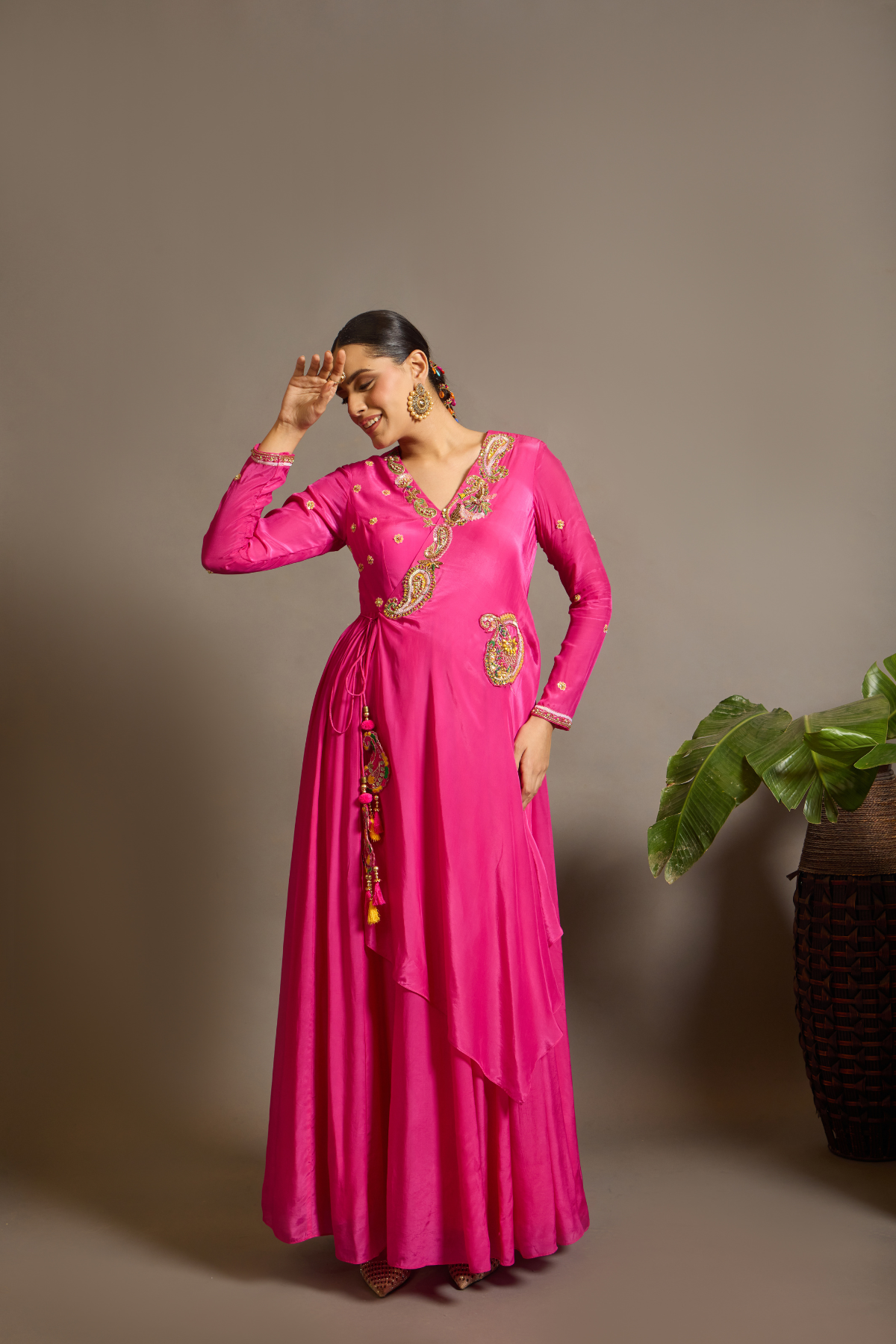 A striking fuchsia-pink Anarkali in a fluid lustrous fabric, designed with an elegant layered flare. Intricate paisley and floral embroidery in multicoloured threadwork enhances the neckline and waist. Handcrafted statement tassels adds festive charm. A vibrant contemporary Silhoutte perfect for festive soirées. Shop Now!