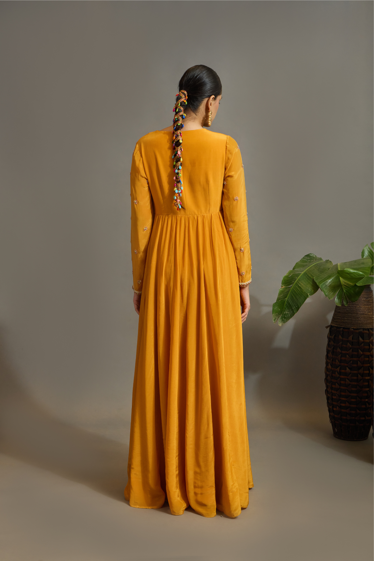 A vibrant marigold-orange Anarkali crafted in a fluid, lustrous fabric with a graceful layered silhouette. Adorned with intricate multicolour paisley embroidery and delicate scattered embellishments. Features a flattering tie-up waist with handcrafted tassels and elegant embroidered work. Shop Now!