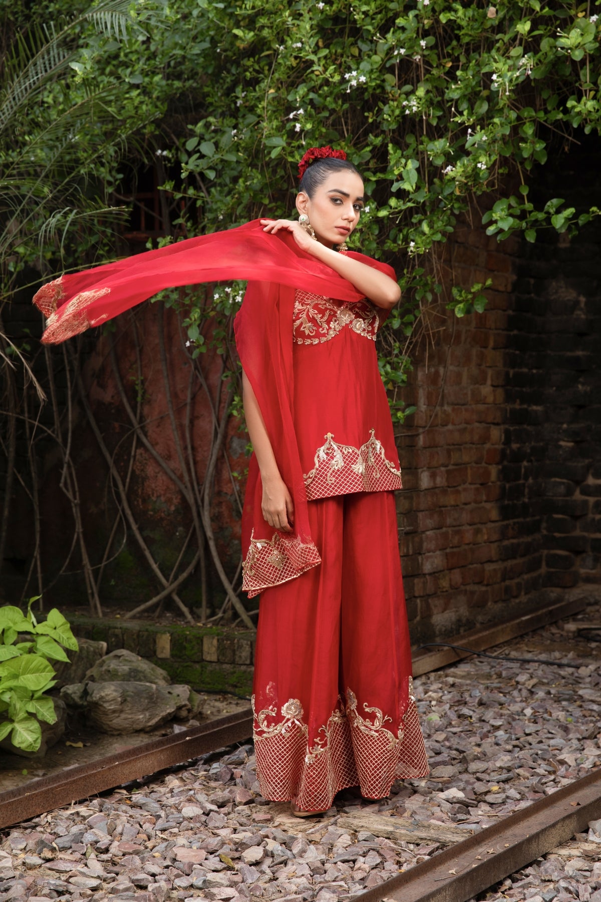 Scarlet red silk corset peplum top with Rococo-inspired hand embellishments, paired with organza palazzo and dupatta featuring zari. Shop Now!
