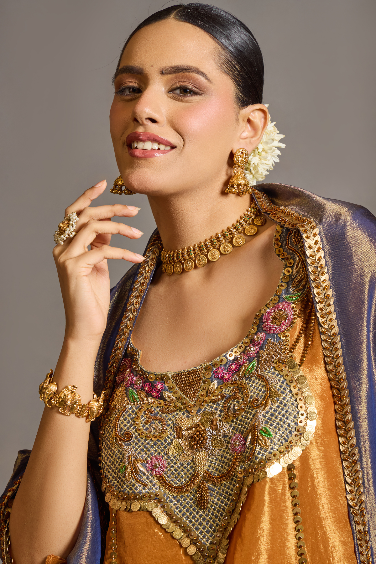 A luminous burnt-orange kurta in a rich metallic finish, elevated with an ornate handcrafted embroidered yoke. The statement neckline features intricate multicolour florals, paisleys,sequins and antique-gold detailing. Layered with a deep-navy blue metallic dupatta finished with ornate borders and delicate embellishment. A festive look that blends contemporary glamour with traditional Indian craftsmanship. Shop Now!
