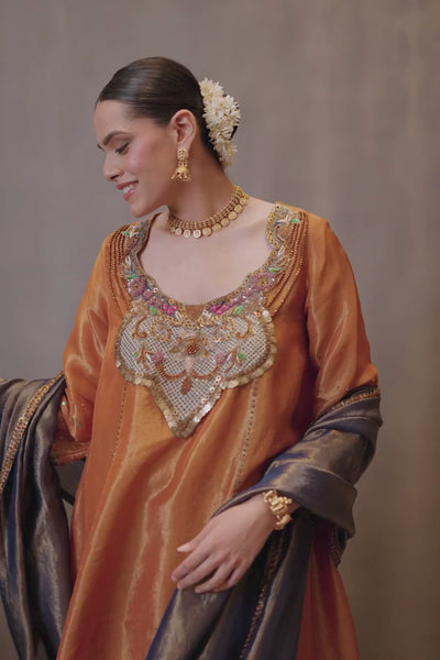 A luminous burnt-orange kurta in a rich metallic finish, elevated with an ornate handcrafted embroidered yoke. The statement neckline features intricate multicolour florals, paisleys,sequins and antique-gold detailing. Layered with a deep-navy blue metallic dupatta finished with ornate borders and delicate embellishment. A festive look that blends contemporary glamour with traditional Indian craftsmanship. Shop Now!