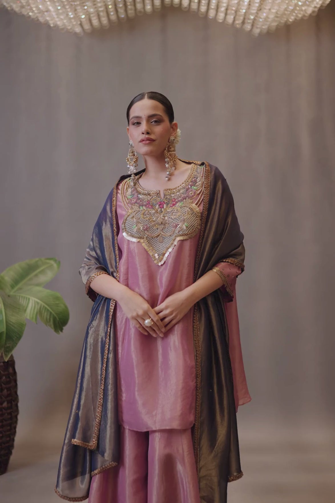 A luminous rose-pink kurta and flared palazzo set crafted in rich,metallic-finish fabric. Featuring an ornate multicolour embroidered neckline with intricate zardozi inspired detailing. Paired with a contrasting deep-blue dupatta finished with elegant gold borders. A festive ensemble that beautifully blends contemporary ease with traditional opulence. Shop Now!