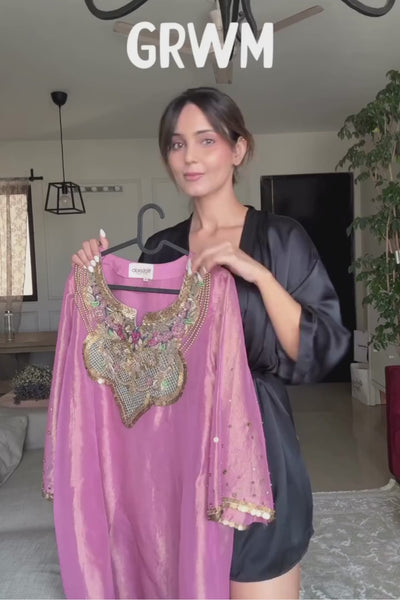 A luminous rose-pink kurta and flared palazzo set crafted in rich,metallic-finish fabric. Featuring an ornate multicolour embroidered neckline with intricate zardozi inspired detailing. Paired with a contrasting deep-blue dupatta finished with elegant gold borders. A festive ensemble that beautifully blends contemporary ease with traditional opulence. Shop Now!